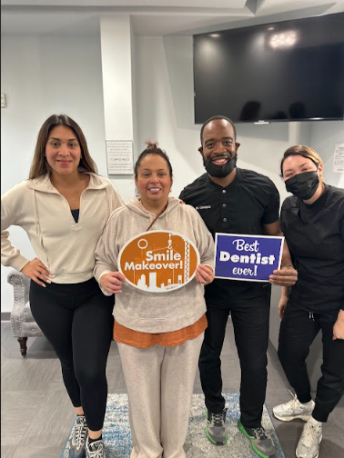A happy dental patient holding a "Smile Makeover!" sign alongside her dentist and dental staff in a Dallas, TX clinic.